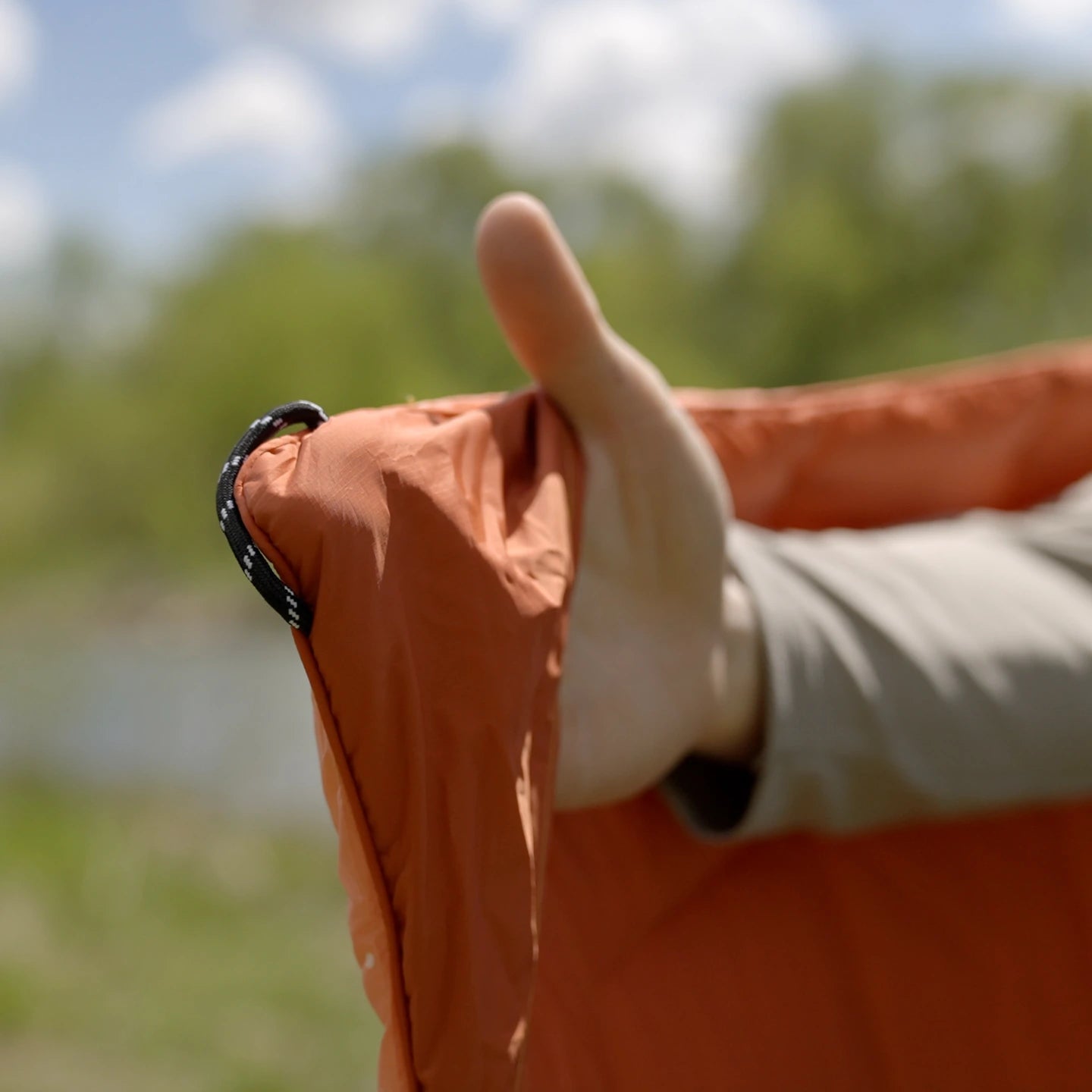 A hand inside the corner pocket of an orange Kukün blanket, beside its braided loop.